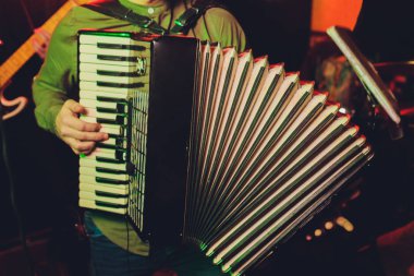 Bir adam kırmızı akordeon çalıyor. Müzik aleti. Restorandaki olay. Siyah yuvarlak düğmeler. El mızıkası.