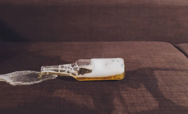 Alcoholism in the family. Beer bottle and spilled beer in the sofa. — Stock Photo, Image
