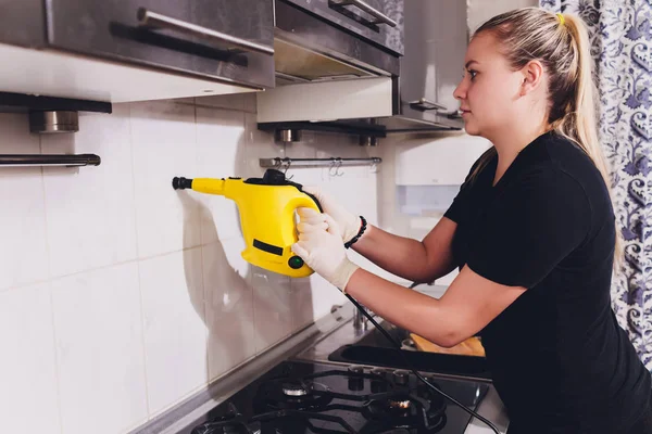 Wanita muda membersihkan dapur dengan pembersih uap . — Stok Foto