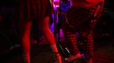 Genç hippi kadın bacakları ve kırmızı gitarın neon ışıklarıyla yakın plan fotoğrafı. Rock müzisyeni elektro gitar çalıyor..