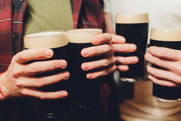 Man groep klinkende glazen van donker en licht bier op baksteen muur achtergrond. — Stockfoto