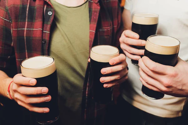 Male group clinking glasses of dark and light beer on brick wall background. — Stock Photo, Image