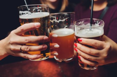 Erkek grubu tuğla duvar arkasında koyu ve hafif bira bardaklarını tokuşturuyor..