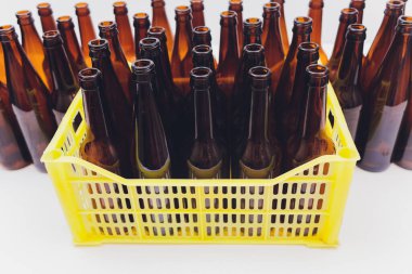 Dusty vintage yellow beer crate with empty brown beer bottles on white background.