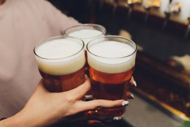 Kadın elinde üç bardak bira barmeni tutuyor..