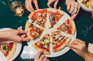 Düz midye, roka ve parmesan ile geleneksel İtalyan pizza koyu mavi taş masa üzerine yatırın. Arkadaşlar pizza yemek. Pizza bir dilim kapma halklar eller.