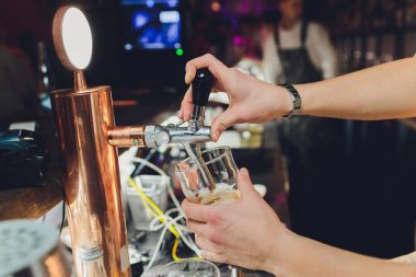 Close up of a male bartender dispensing draught beer in a pub holding large glass tankard under a spigot attachment on a stainless steel keg.