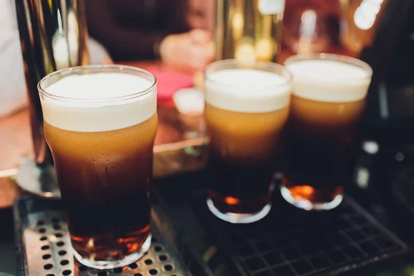 Närbild på en manlig bartender dispensering öl på en pub som innehar ett stort glas tankard under en tapp fastsättning på ett rostfritt stål fat. — Stockfoto