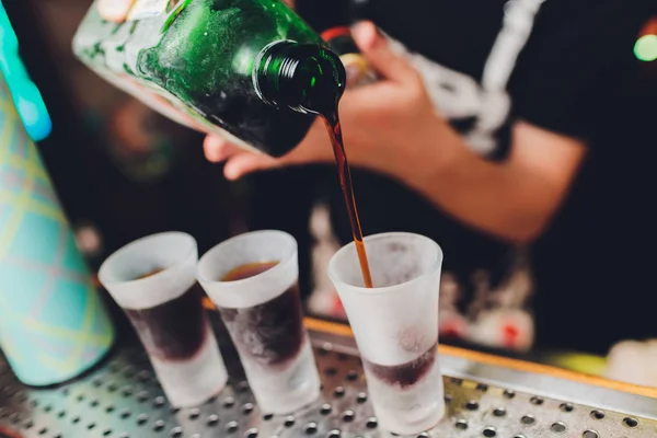 Barman leje silny napój alkoholowy, w niewielkich kieliszkach na pasek, zdjęcia. — Zdjęcie stockowe
