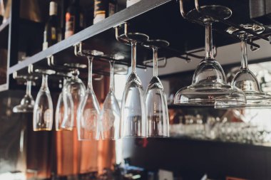 Closeup çok baş aşağı boş şeffaf şeffaf kristal ters şarap bardakları kahverengi ahşap raf, raf, vitrin, paslanmaz çelik korkuluk barda düz sıralar asılı, dolap.