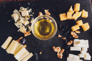 Yuvarlak ahşap tabakta çeşitli peynirler Camembert peyniri, peynir rendelenmiş meşe kabuğu, sert peynir dilimleri, cevizler, üzümler, krakerler, ekmek, kekik, koyu siyah ahşap arka plan, üst görünüm..
