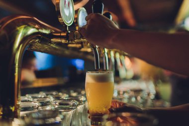 erkek bir barmen büyük cam tankerin altında spigot ek bir Paslanmaz Çelik varil üzerinde tutan bir barda fıçı bira dağıtımı, yakın çekim.