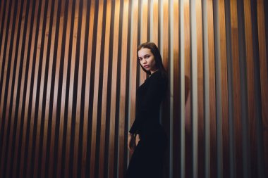 Young girl walks past a wooden wall stops and looks into the camera. Portrait of a beautiful long-haired girl in the background a wooden wall.