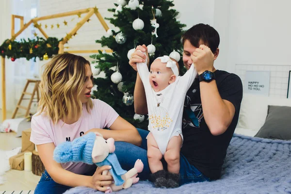 Familie zit met de baby zit in de buurt van de kerstboom, de baby een jaar oud is en een jonge vrouw en een man wachten voor Kerstmis. — Stockfoto