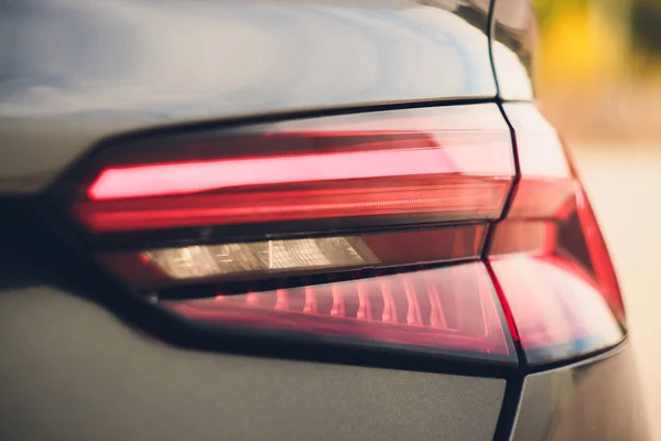 Detalhe do farol traseiro preto metalizado vermelho do carro na forma do olho, com reflexão do sol na pupila . — Fotografia de Stock