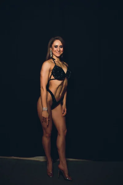 Mujer joven atlética muscular en traje de baño de color sobre fondo negro. Fitness. Cuerpo muscular. Torso. Músculos abdominales —  Fotos de Stock