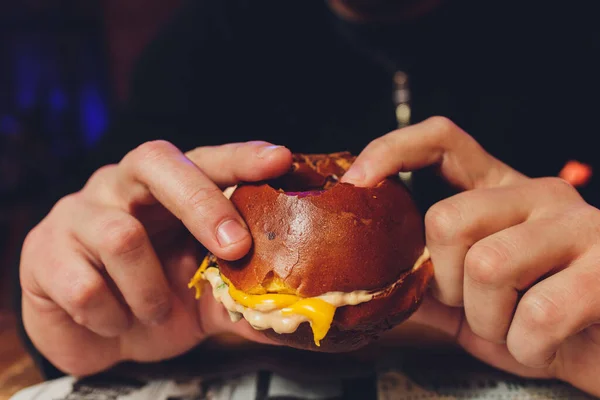 A bitten fresh burger in the hands of a man.