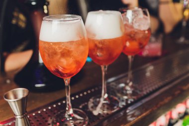 Kırmızı acı tonik, limon ve buzlu Campari tonik kokteyli. Eski ahşap masa arkaplanı, bar araçları, seçici odaklanma. Tüm isimler kokteyllere yöneliktir, markalara değil..