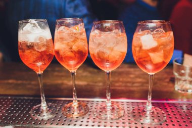 Kırmızı acı tonik, limon ve buzlu Campari tonik kokteyli. Eski ahşap masa arkaplanı, bar araçları, seçici odaklanma. Tüm isimler kokteyllere yöneliktir, markalara değil..