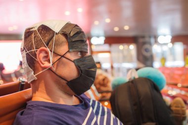 Yüzünde tıbbi maske olan bir adam havaalanında oturuyor ve elinde bir telefon tutuyor. Çin 'de Coronavirus. Salgın tehdidi var. Boşluğun kopyası.