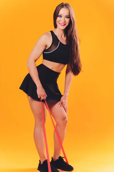 Ragazza atletica esegue esercizi utilizzando una fascia di resistenza. Foto di giovane ragazza sullo sfondo. Forza e motivazione . — Foto Stock