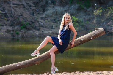 Mavi mini elbisesi ve çiçekli çelengi olan genç, sarışın bir kadın yaz günü arka planda kırsal alanda su arıyormuş. Kadın doğal güzellik ve yaz doğa kavramı.