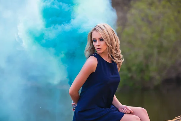 Junge schöne blonde Frau in blauem Minikleid und Blumenkranz steht und probiert Wasser an einem Sommertag mit Landschaft im Hintergrund. Frau natürliche Schönheit und Sommer-Natur-Konzept. Rauch — Stockfoto