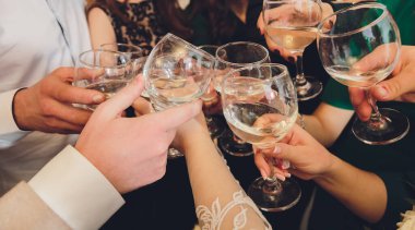 Bokeh arkaplanının önünde kadeh tokuşturup şampanya içen bir grup insanı yakından çek. Yaşlı insanların elleri.