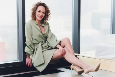 Gri duvar arkasında kolları çapraz duran yeşil elbiseli güzel kızıl saçlı genç bir bayan resmi. Kameraya bak.