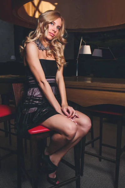 Mujer bonita en vestido de noche negro, con el estilo de pelo posando cerca de un bar restaurante, mirando en la cámara  . — Foto de Stock