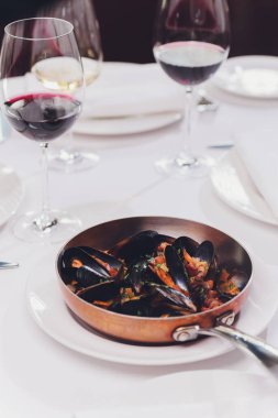 Beyaz zemin üzerinde kaynamış midyeler bakır yemek kabında yakın plan.