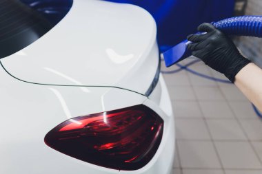 Yakından çekilmiş bir portre, mavi gömlekli genç bir adam, yıkandıktan sonra gümüş hortumla arabasını kurutuyor. Pahalı boya ve krom için güvenli. Balmumunun bozulmamasını sağlayan daha az işlem..