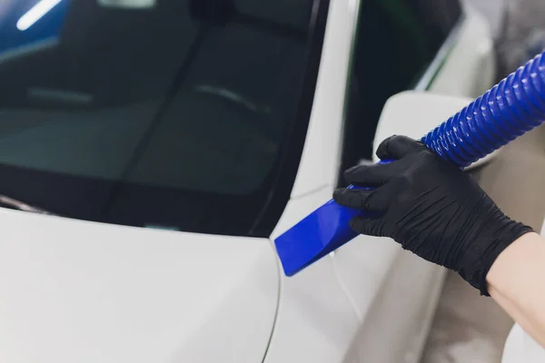 Retrato de primer plano, joven conductor de camisa azul, secando al aire su coche plateado con manguera de vacío después del lavado. Seguro para pintura costosa y cromo. Un proceso sin tacto que mantiene intacta la cera . — Foto de Stock