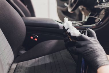 Eldivenli işçi araba koltuğunu fırçayla yıkıyor..