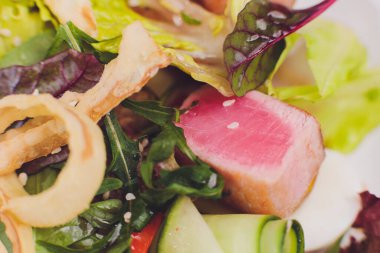 Kurutulmuş ton balığı kaplı susam tohumları ve beyaz tabakta yeşil salata..