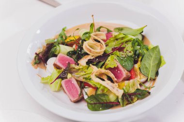 Kurutulmuş ton balığı kaplı susam tohumları ve beyaz tabakta yeşil salata..