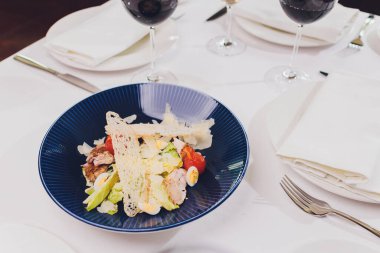 Kırsal arka planda mavi tabakta tavuklu Sezar salatası.