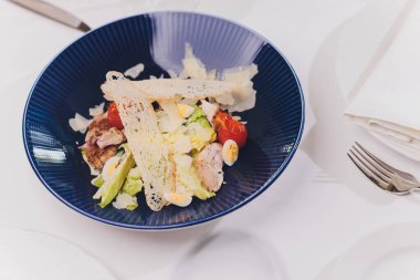 Kırsal arka planda mavi tabakta tavuklu Sezar salatası.