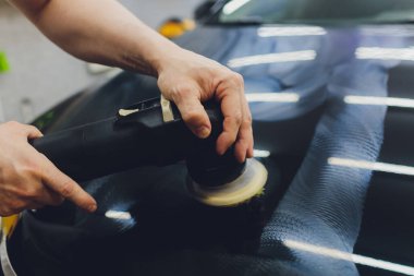 Yörüngesel cilalayıcısı olan bir adam tamir atölyesinde araba parlatıyormuş. Seçici odak.