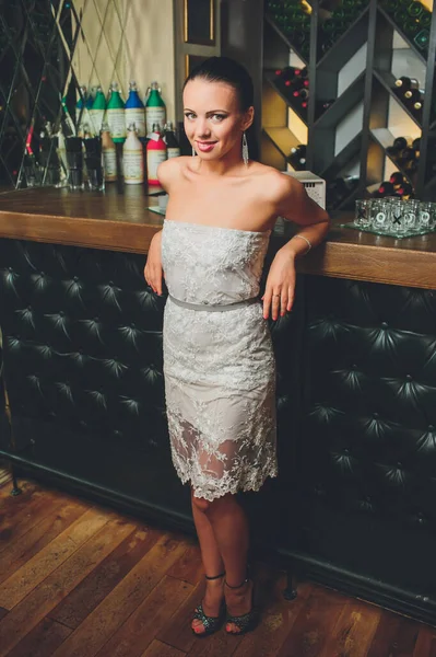 Pretty woman in evening dress , with hair style posing near a restaurant bar, looking in camera. — Stock Photo, Image