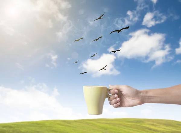 Yeşil kahve fincanı kuş gökyüzü arka plan üzerinde tutan el. — Stok fotoğraf