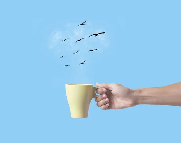 Hand som håller grön kaffekopp med fågel på blå bakgrund. — Stockfoto