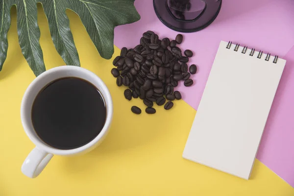 Vista superior plano de la taza de café con cuaderno en blanco, grano de café — Foto de Stock