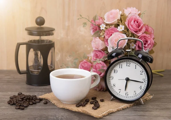 Hot cup of coffee and alarm clock on wood table with rose flower — Stock Photo, Image