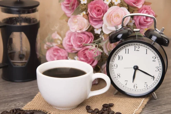 Hot cup of coffee and alarm clock on wood table with rose flower — Stock Photo, Image