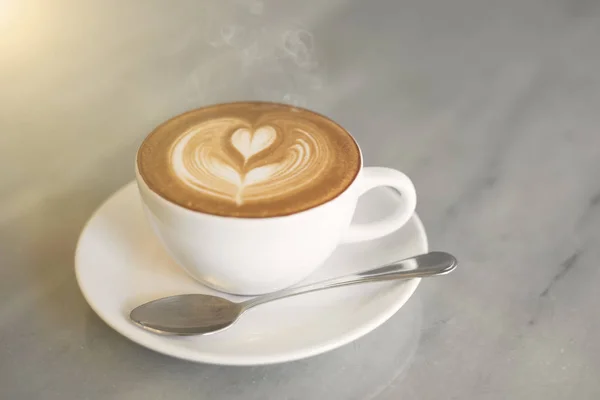 Primer plano café caliente latte arte taza con humo en la mesa . — Foto de Stock