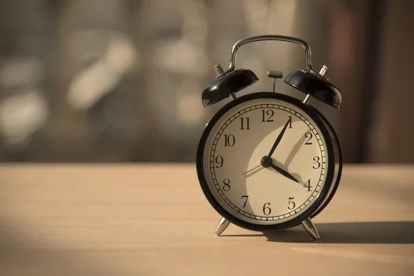 朝の木製テーブルの上の黒の目覚まし時計. — ストック写真