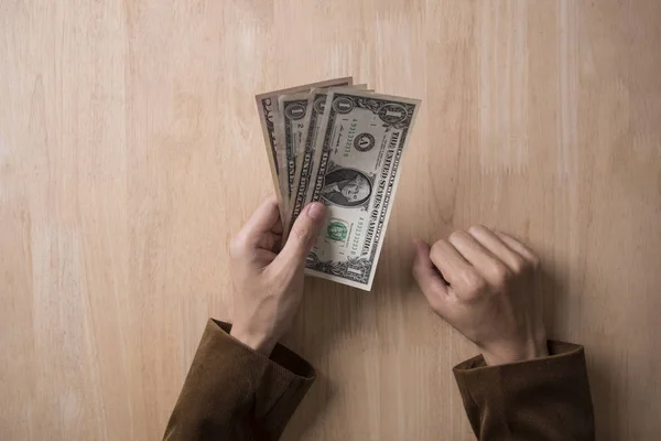 Businessman hand holding dollar on wooden table in office. — Stock Photo, Image