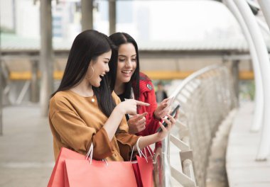 Güzel kızlar alışveriş torbaları bir akıllı telefon kullanarak holding 