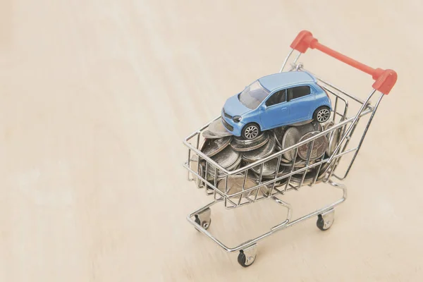 money coin and car in shopping cart on wood table. auto loan